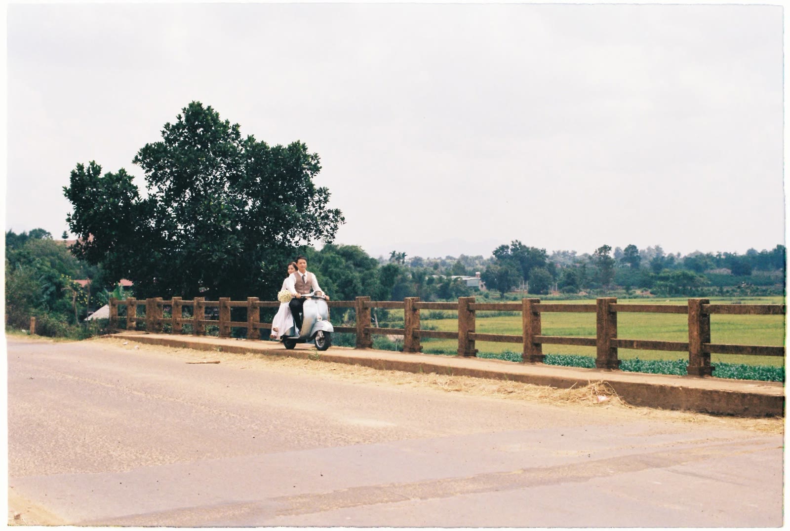 Cặp đôi trên chiếc Vespa chạy qua cây cầu giữa đồng